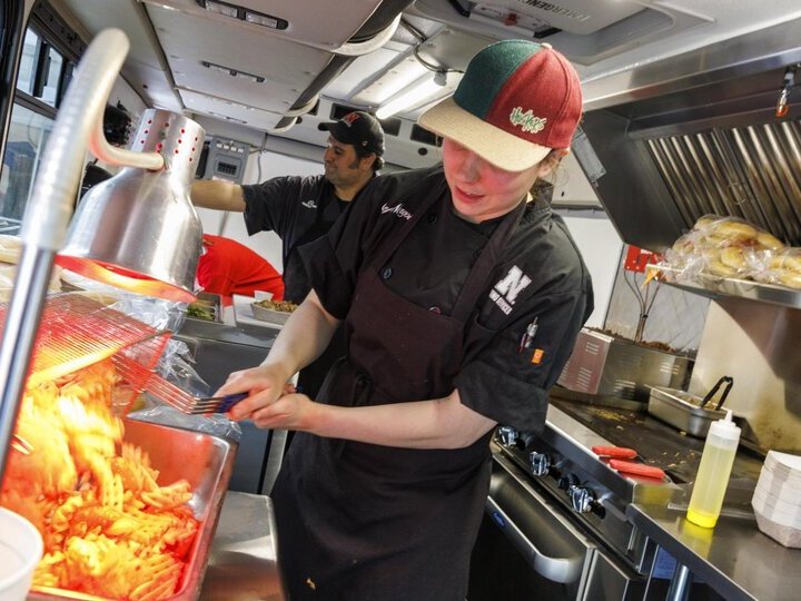 Cooks in harpers food truck pouring freshly deep fried french fries into a container.